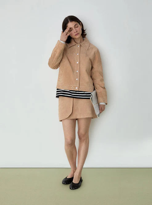 Woman wearing a beige jacket and skirt with a striped top against a white background