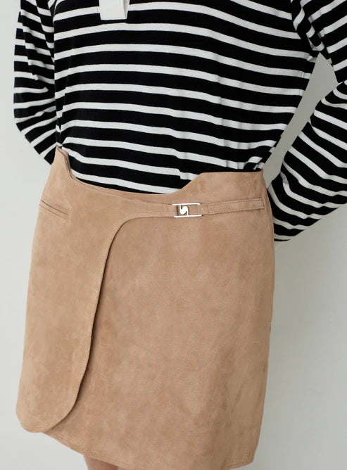 Close-up of a tan wrap-style mini skirt with a metal clasp, worn with a black-and-white striped top.