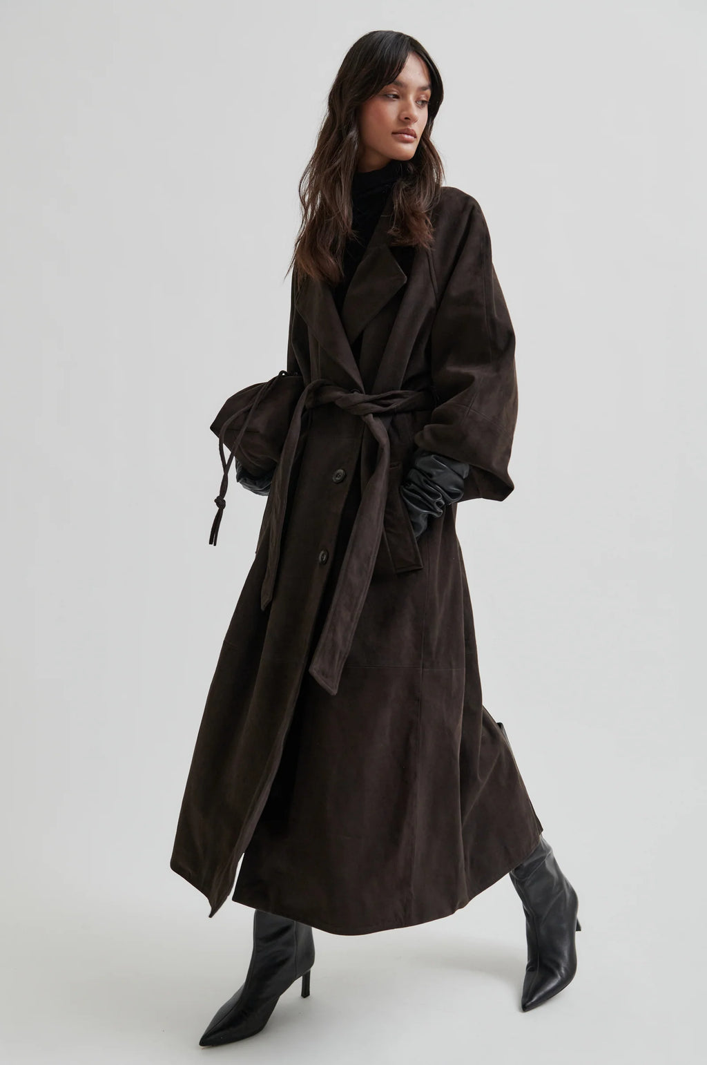 Woman wearing a long dark brown trench coat on a white background