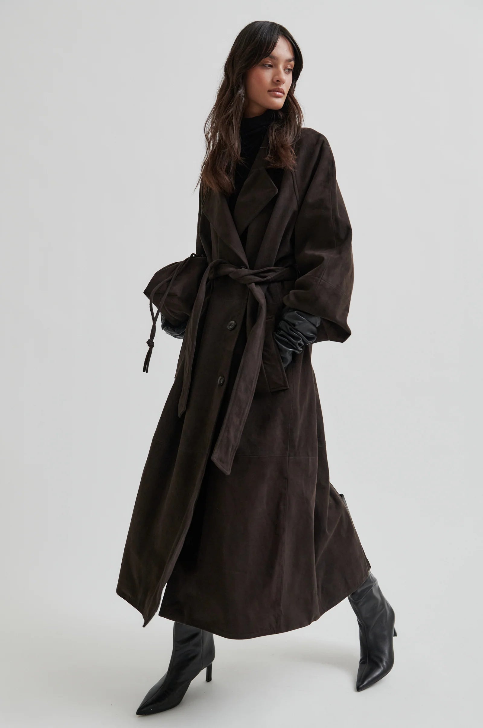 Woman wearing a long dark brown trench coat on a white background