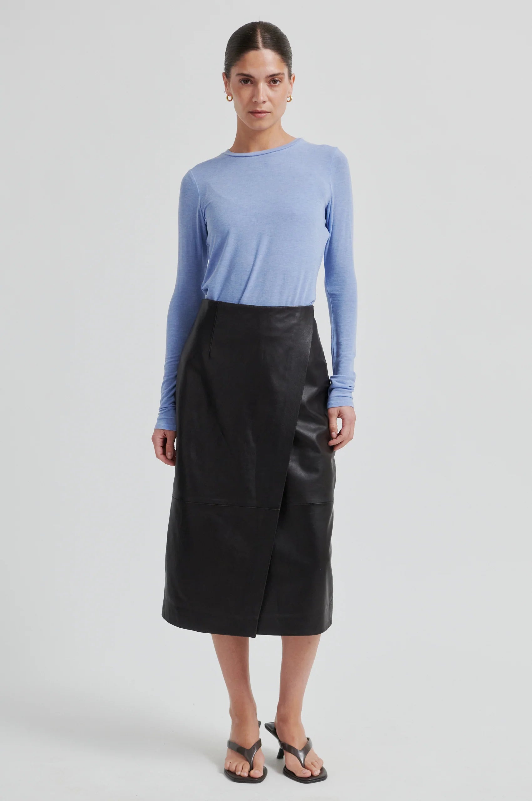 Woman wearing chocolate leather skirt and a blue long-sleeve shirt on a white background