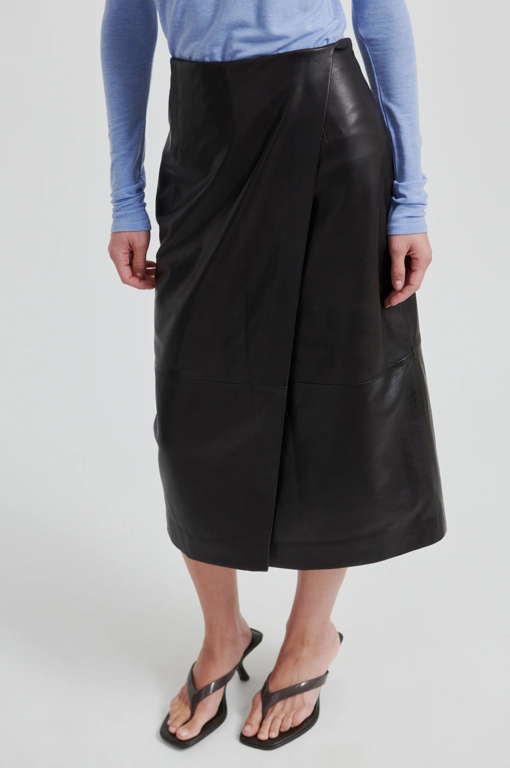 Woman wearing chocolate leather skirt and a blue long-sleeve shirt on a white background