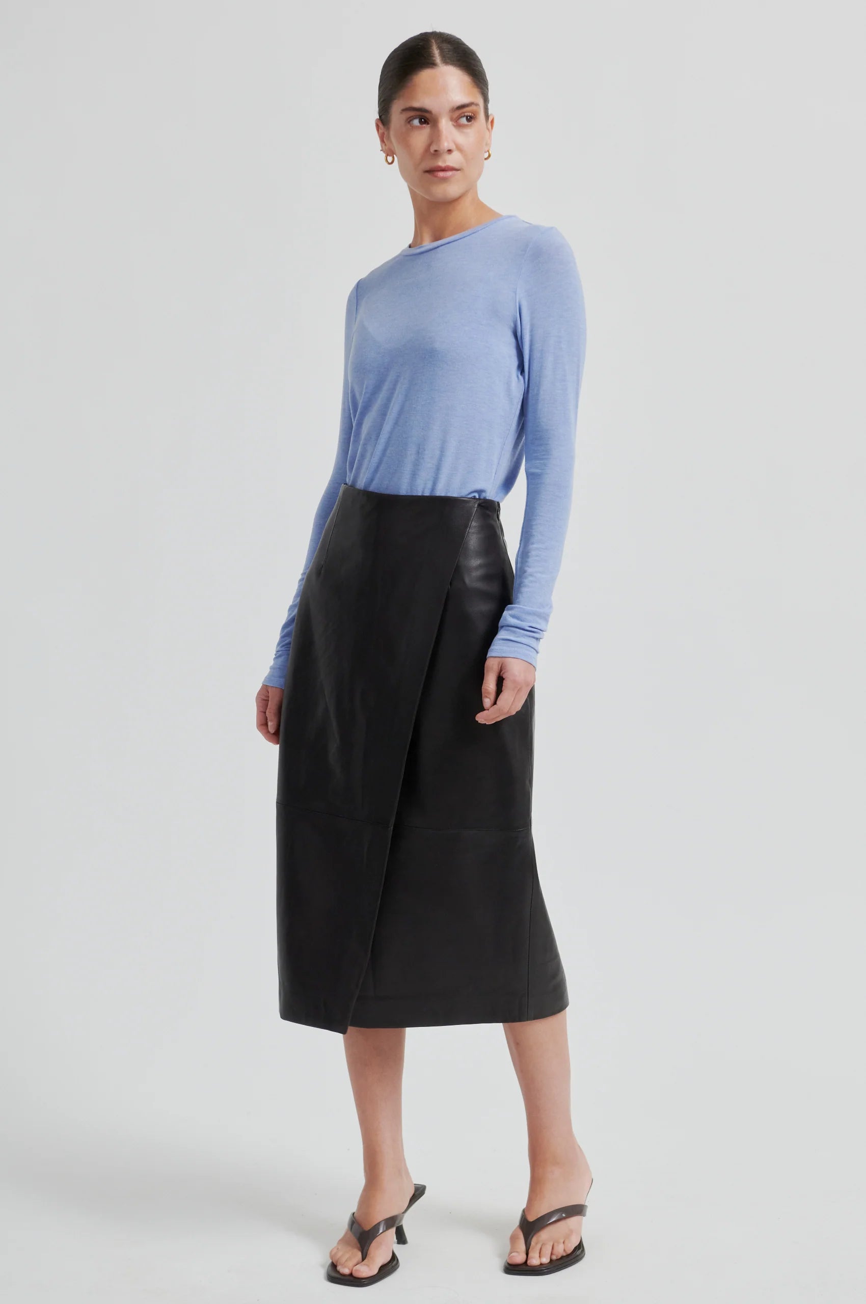 Woman wearing chocolate leather skirt and a blue long-sleeve shirt on a white background