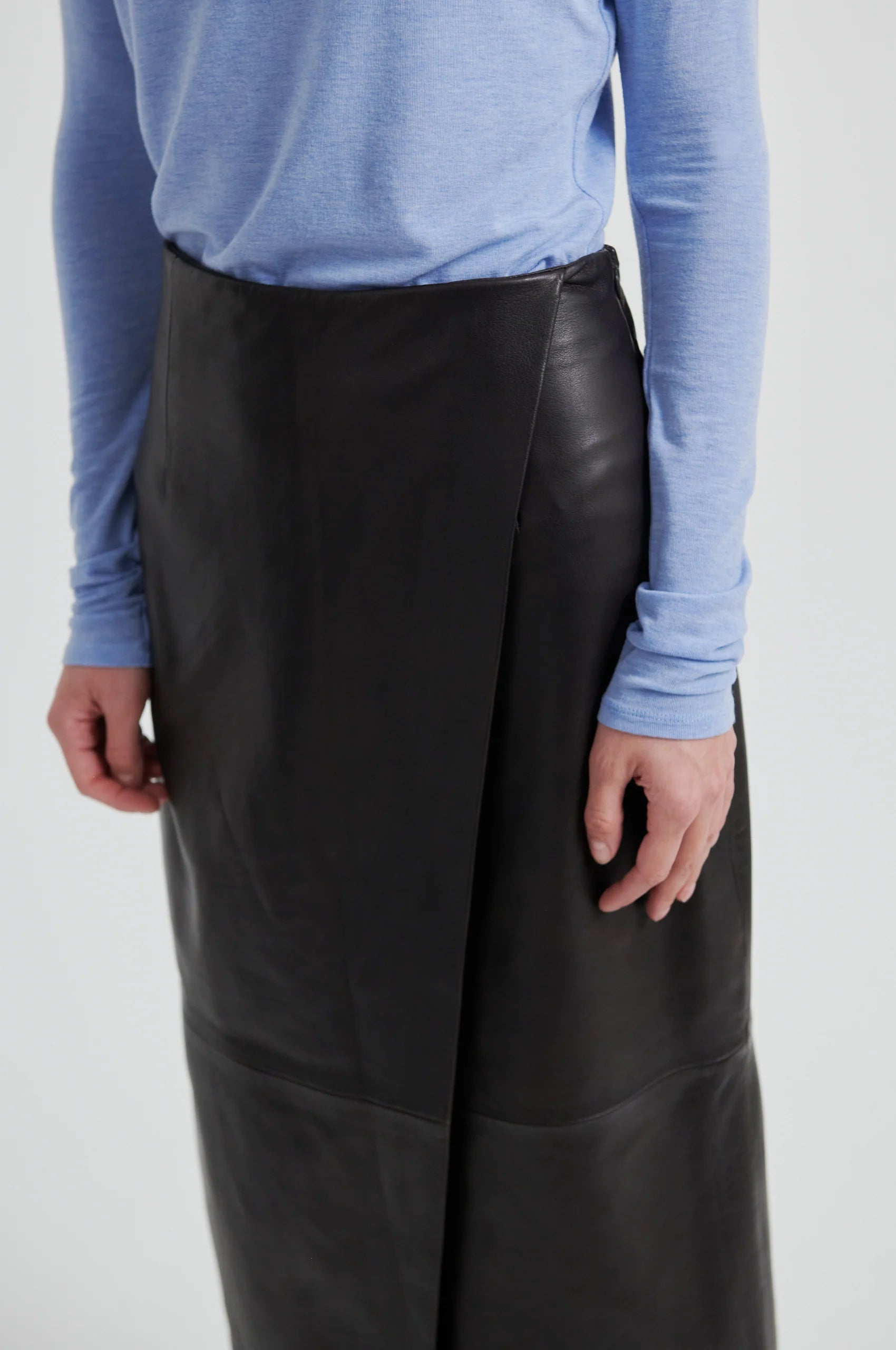 Person wearing chocolate leather skirt and a blue long-sleeve shirt on a white background