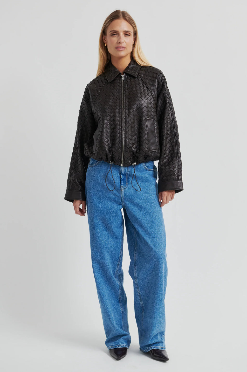 Person wearing a textured chocolate-brown leather jacket with blue jeans against a gray background.