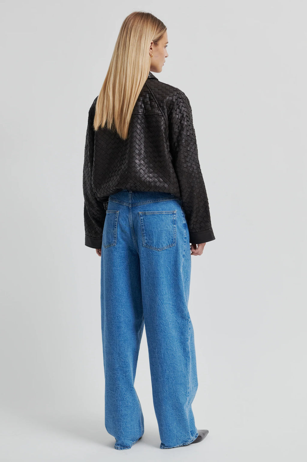 Person wearing a textured chocolate-brown leather jacket with blue jeans against a gray background.