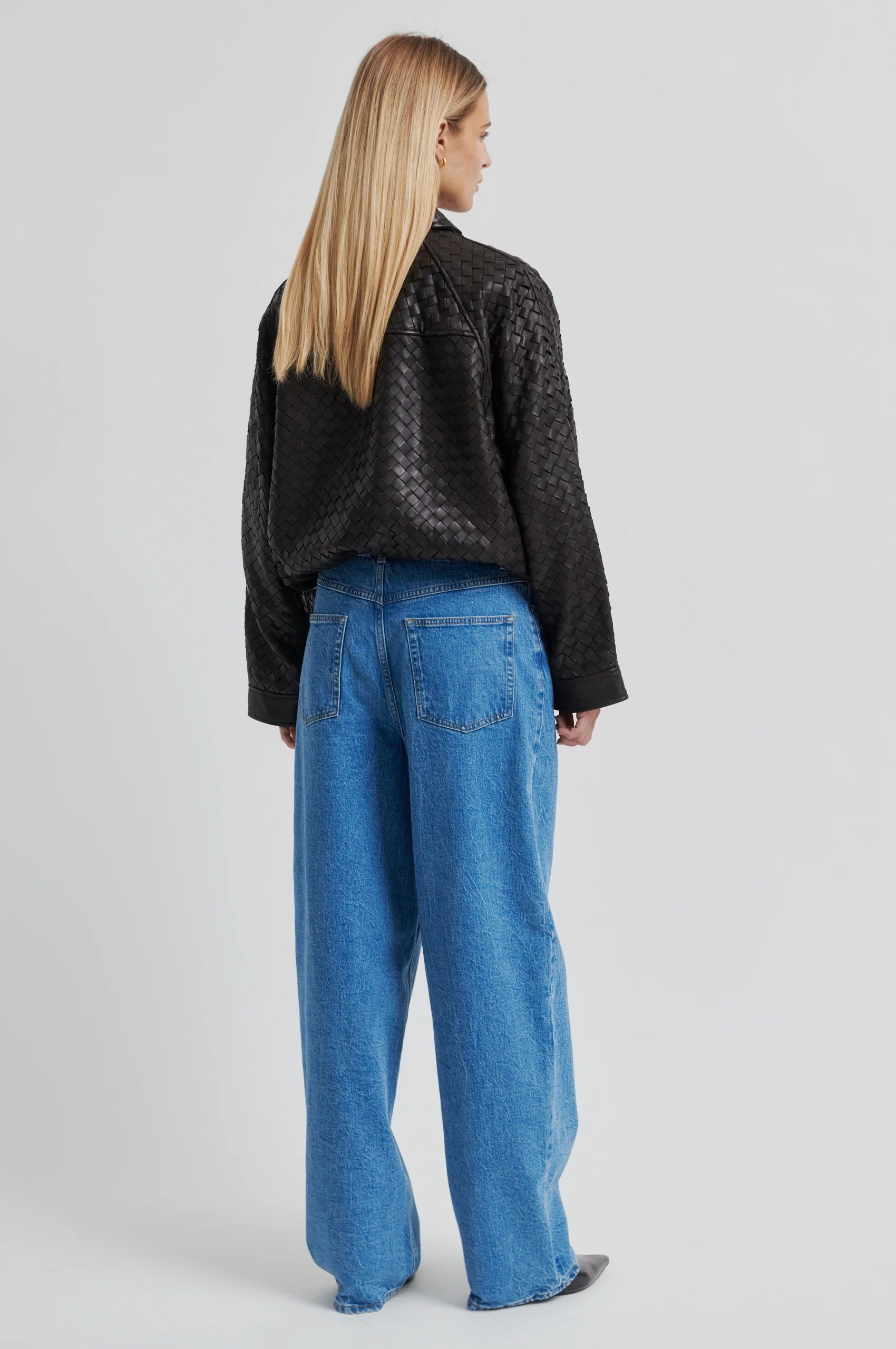 Person wearing a textured chocolate-brown leather jacket with blue jeans against a gray background.