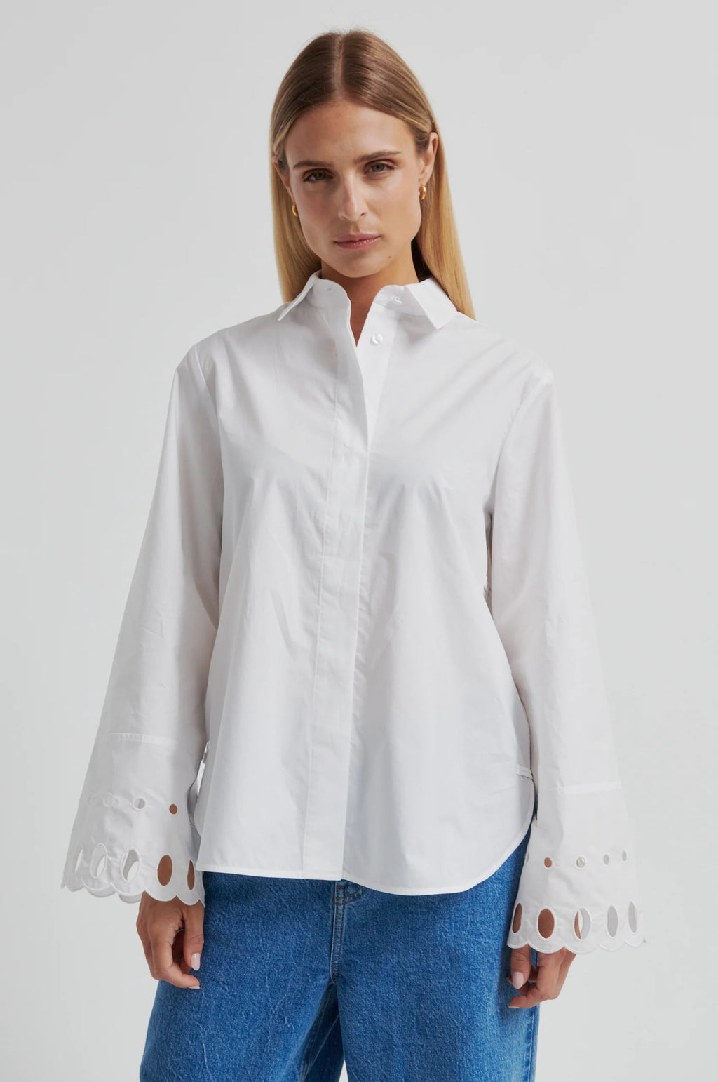 Woman wearing a white shirt with cut-out details on the sleeves against a gray background