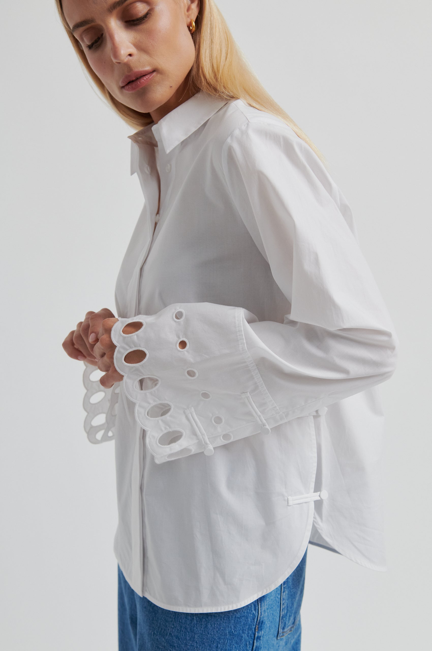 Woman wearing a white shirt with cut-out details on the sleeves against a gray background