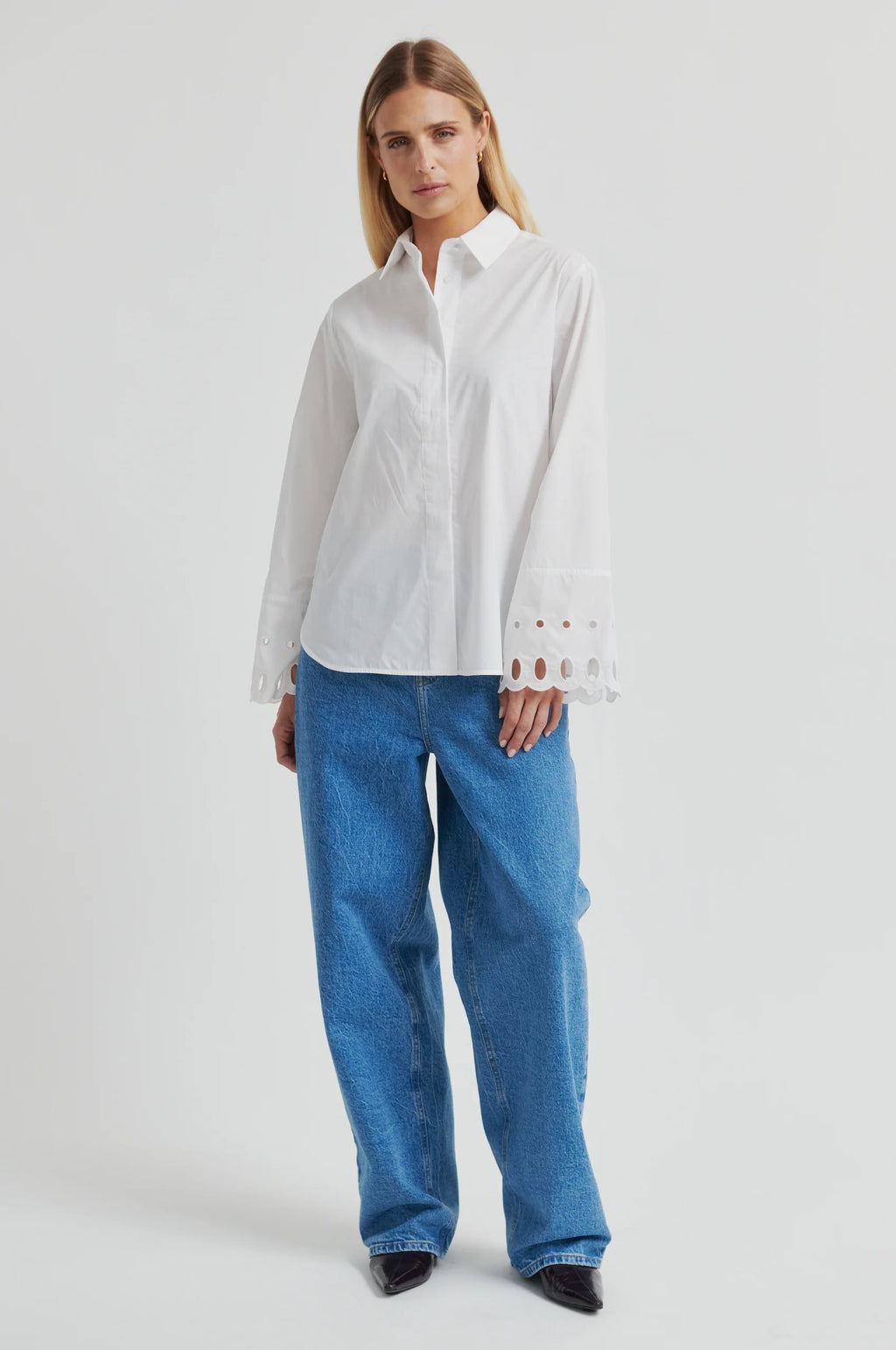 Woman wearing a white shirt with cut-out details on the sleeves against a gray background