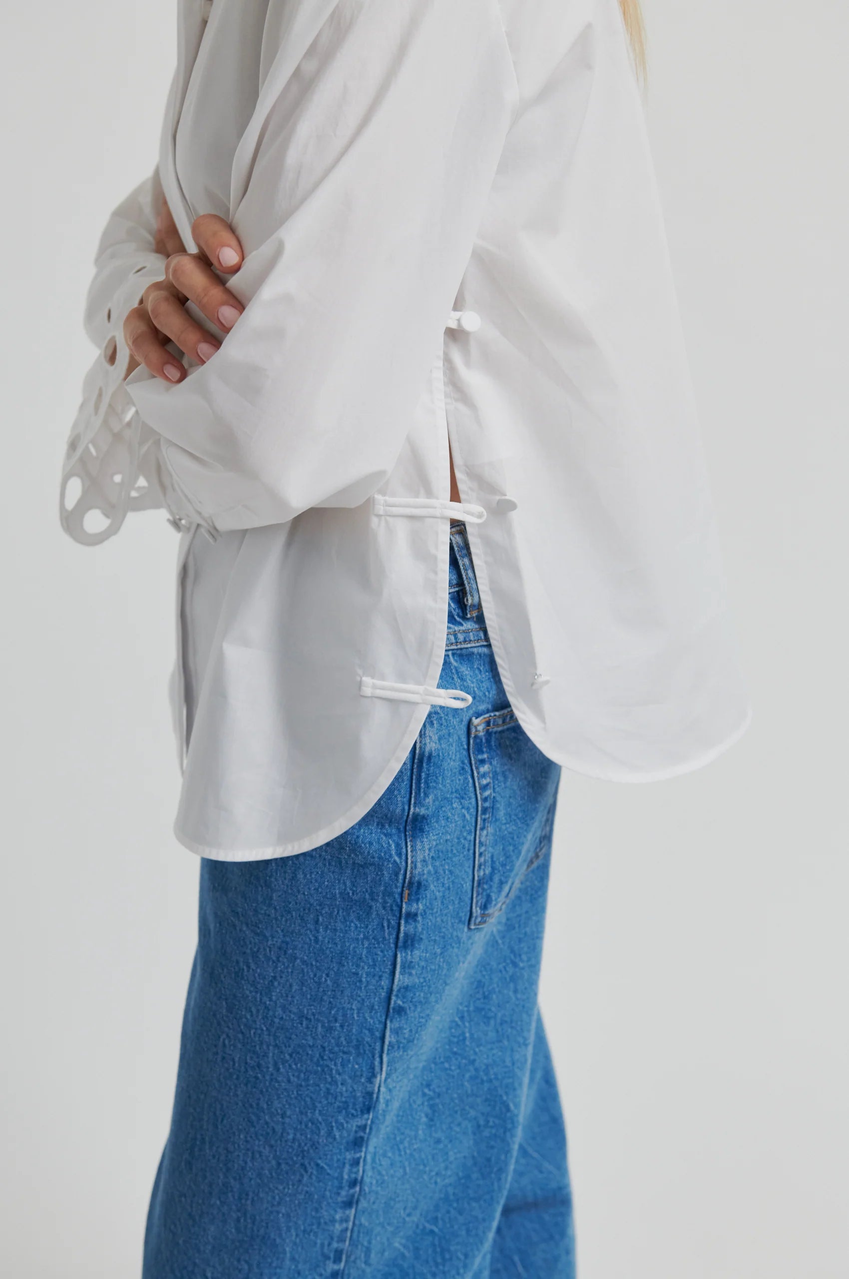 Woman wearing a white shirt with cut-out details on the sleeves against a gray background