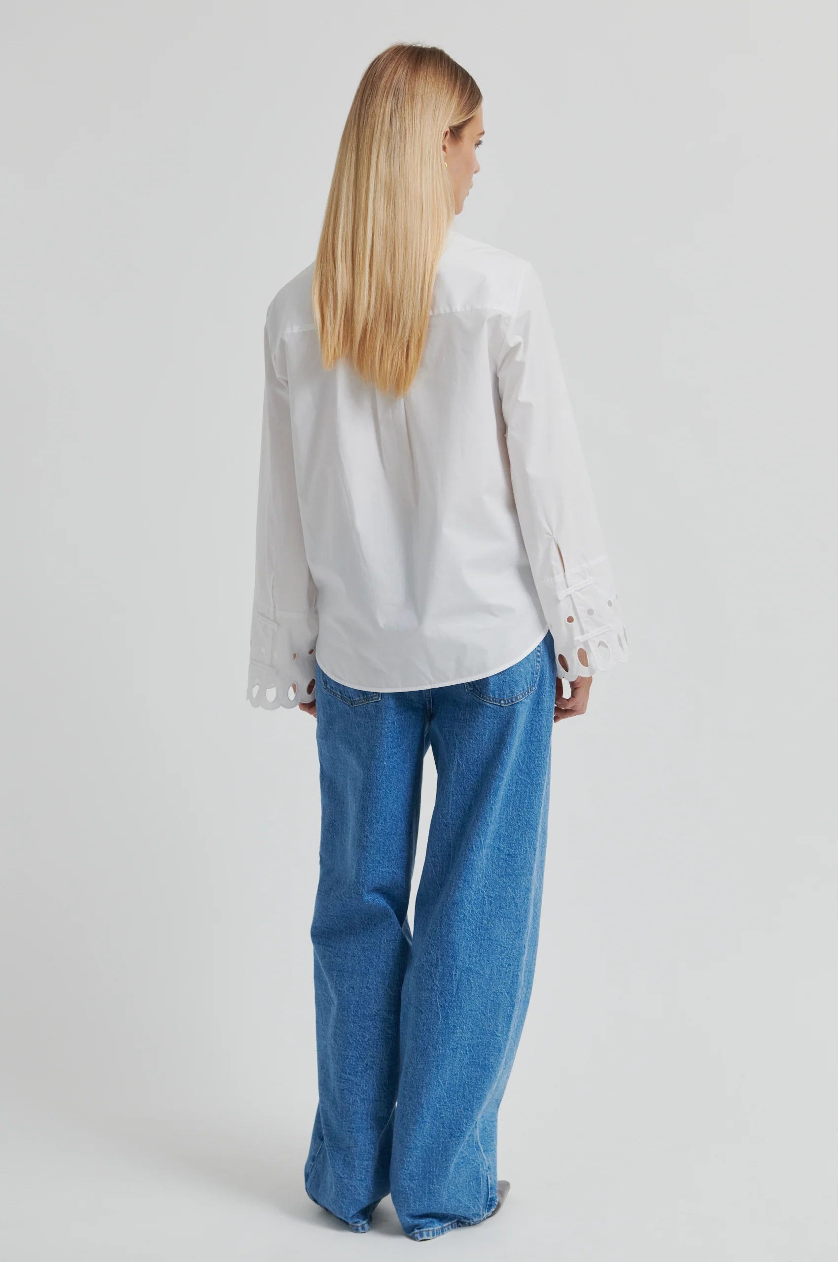 Woman wearing a white shirt with cut-out details on the sleeves against a gray background