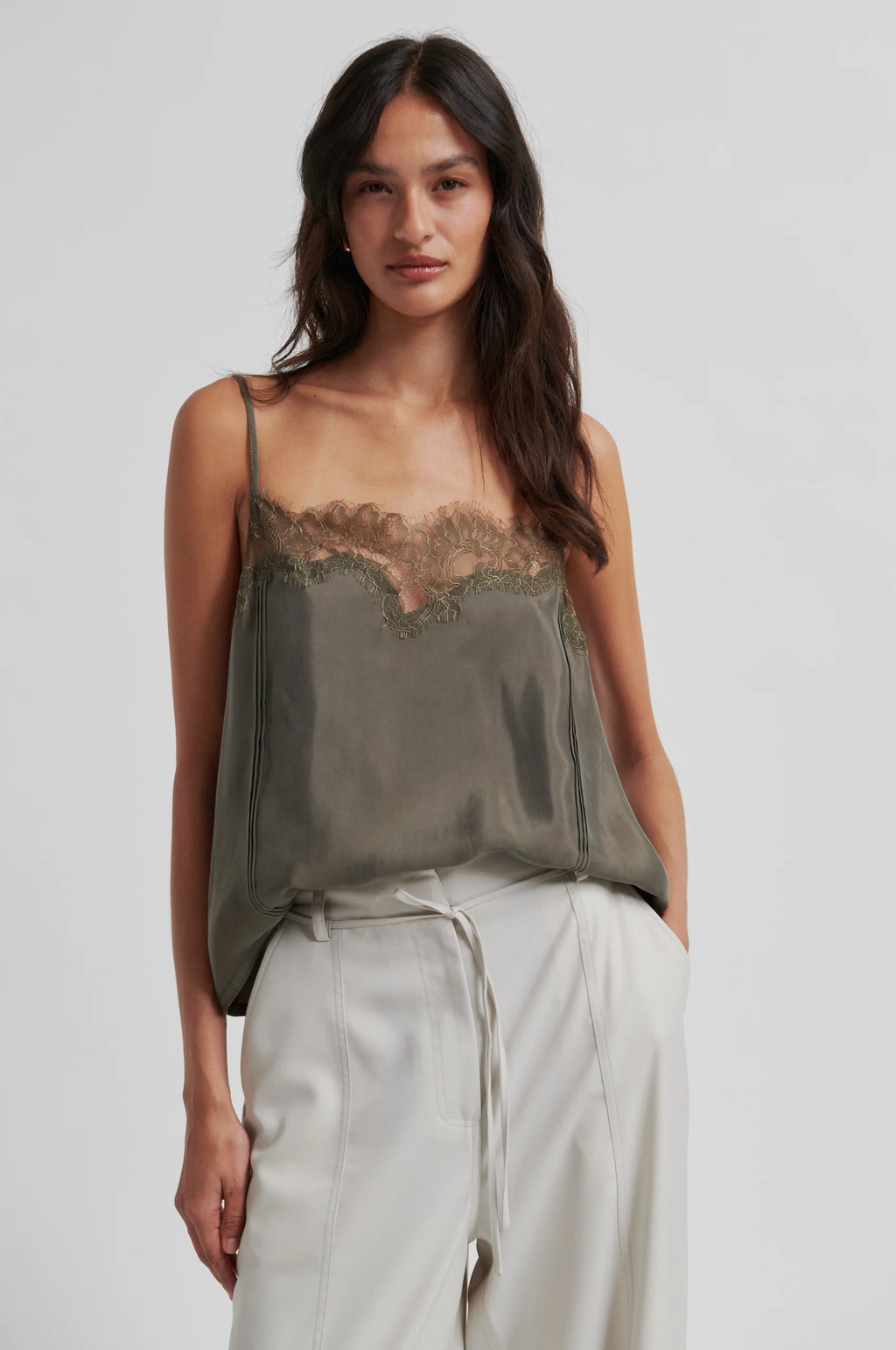 Woman wearing a green lace-trimmed top and light pants on a grey background