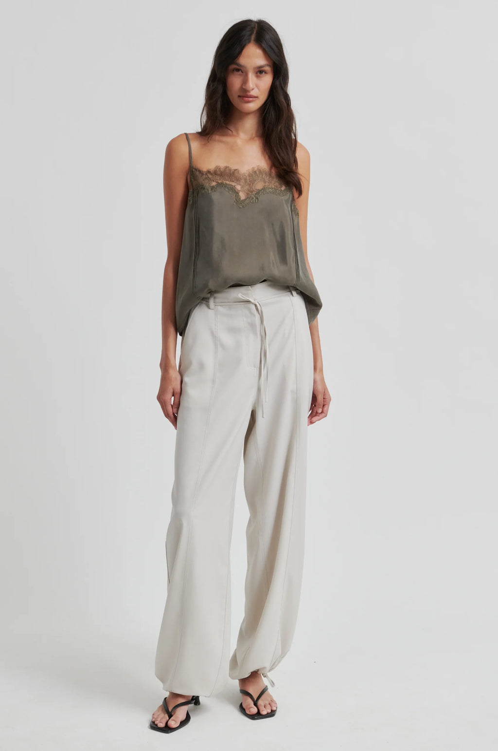 Woman wearing a green top and light-colored pants on a white background