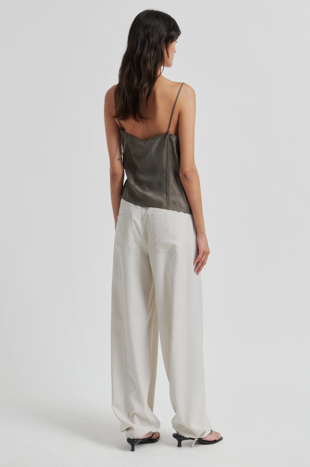 Woman wearing a green satin top and white wide-leg pants on a white background