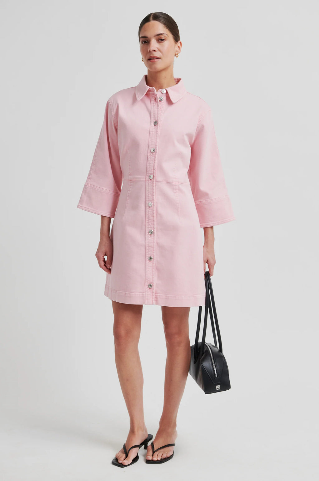 Woman wearing a light pink button-front dress with three-quarter sleeves, standing against a plain background.