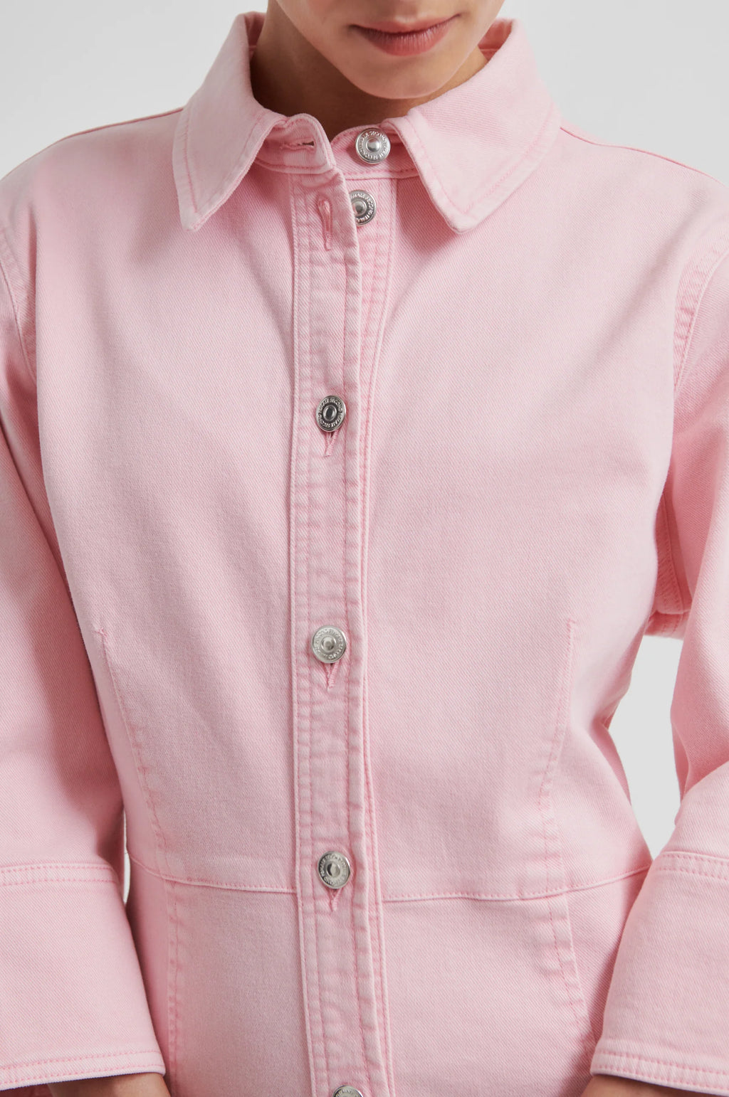 Close-up of a light pink button-front dress with three-quarter sleeves with a white background.