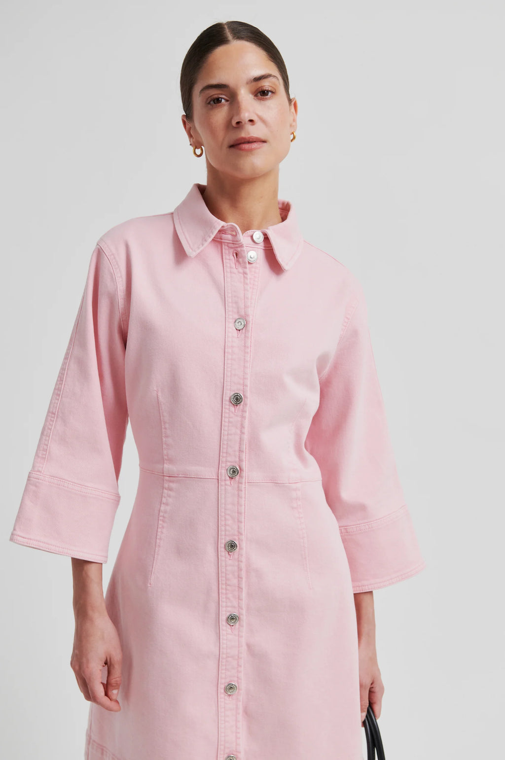 Woman wearing a light pink button-front dress with three-quarter sleeves, standing against a plain background.