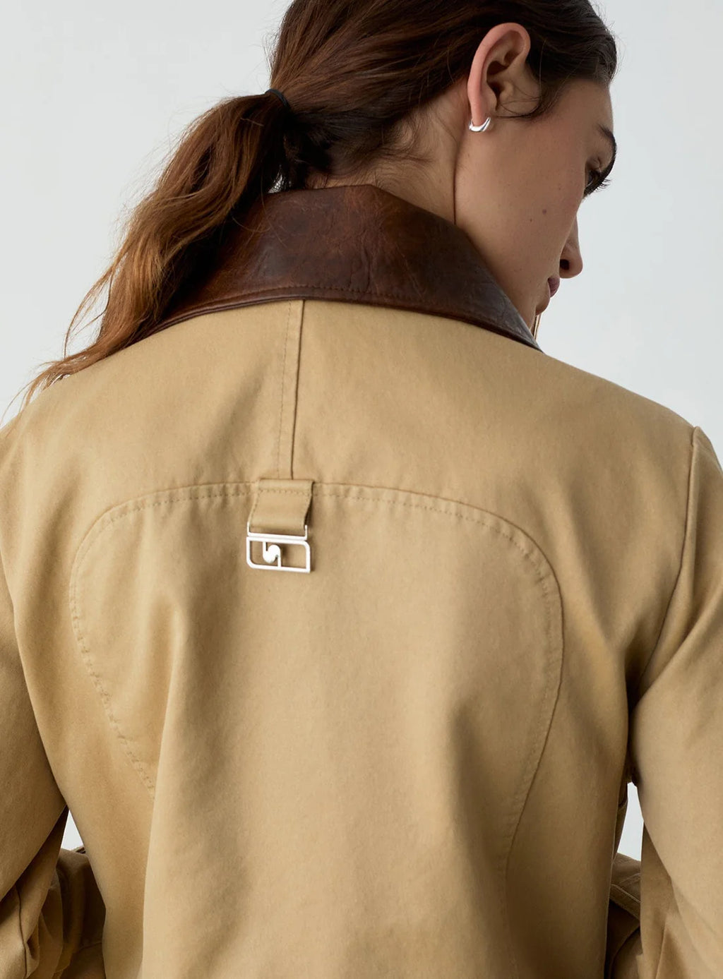 Close-up back view of a woman wearing a tan jacket with a brown leather collar and a small metal clasp detail