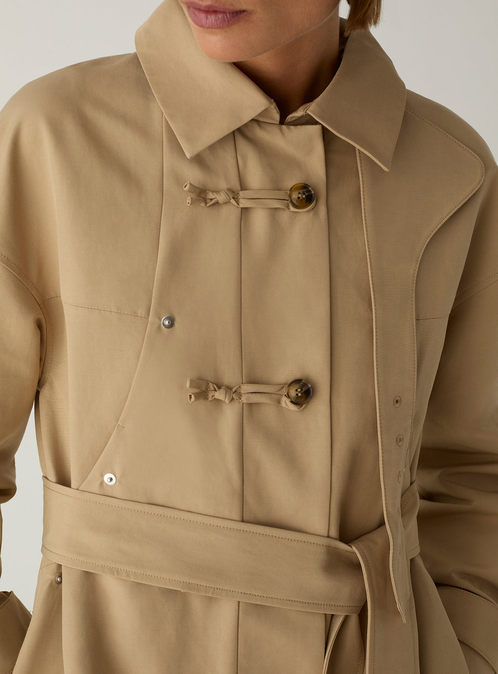The LAAGAM Antwerp camel trench worn with the collar folded open, showing the knotted toggles and self-fabric belt.