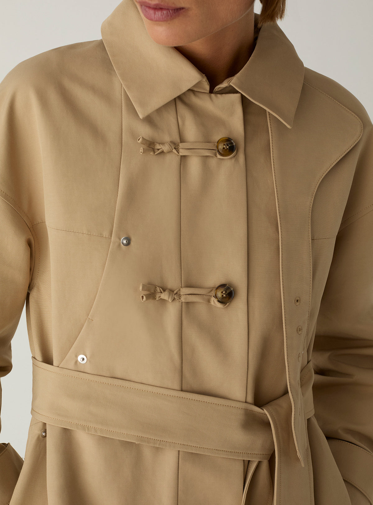 The LAAGAM Antwerp camel trench worn with the collar folded open, showing the knotted toggles and self-fabric belt.