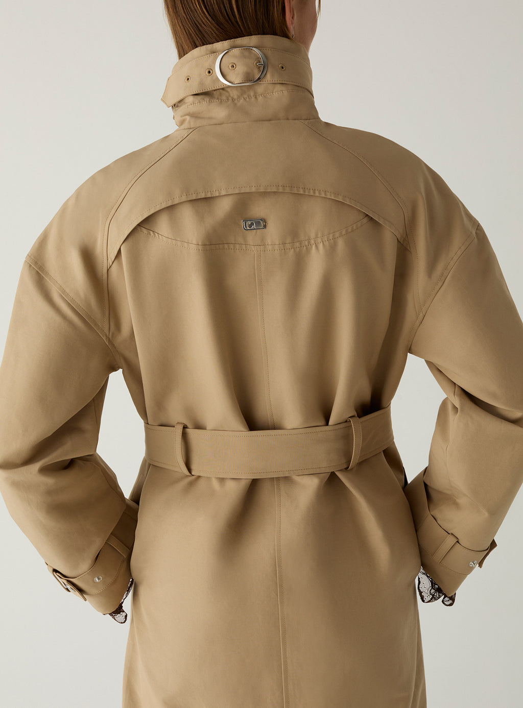 Back of the LAAGAM Antwerp camel trench: buckled collar strap, curved yoke with metal logo plate and belt tied at the waist.