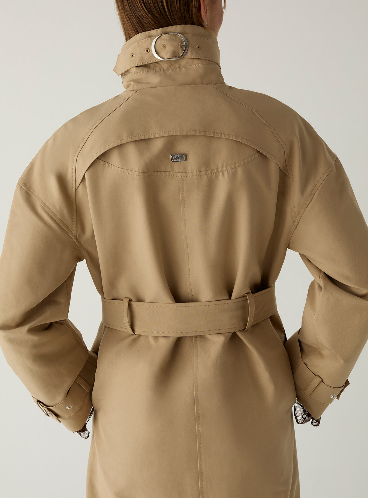 Back of the LAAGAM Antwerp camel trench: buckled collar strap, curved yoke with metal logo plate and belt tied at the waist.