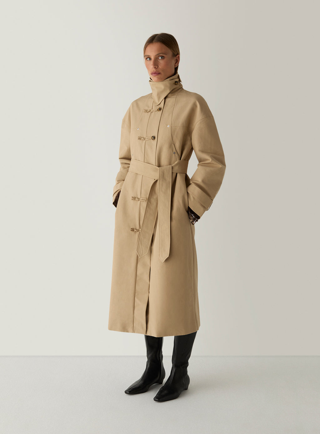 Model in the camel Antwerp trench coat by LAAGAM, collar buttoned up and belt left untied, worn with black knee boots.