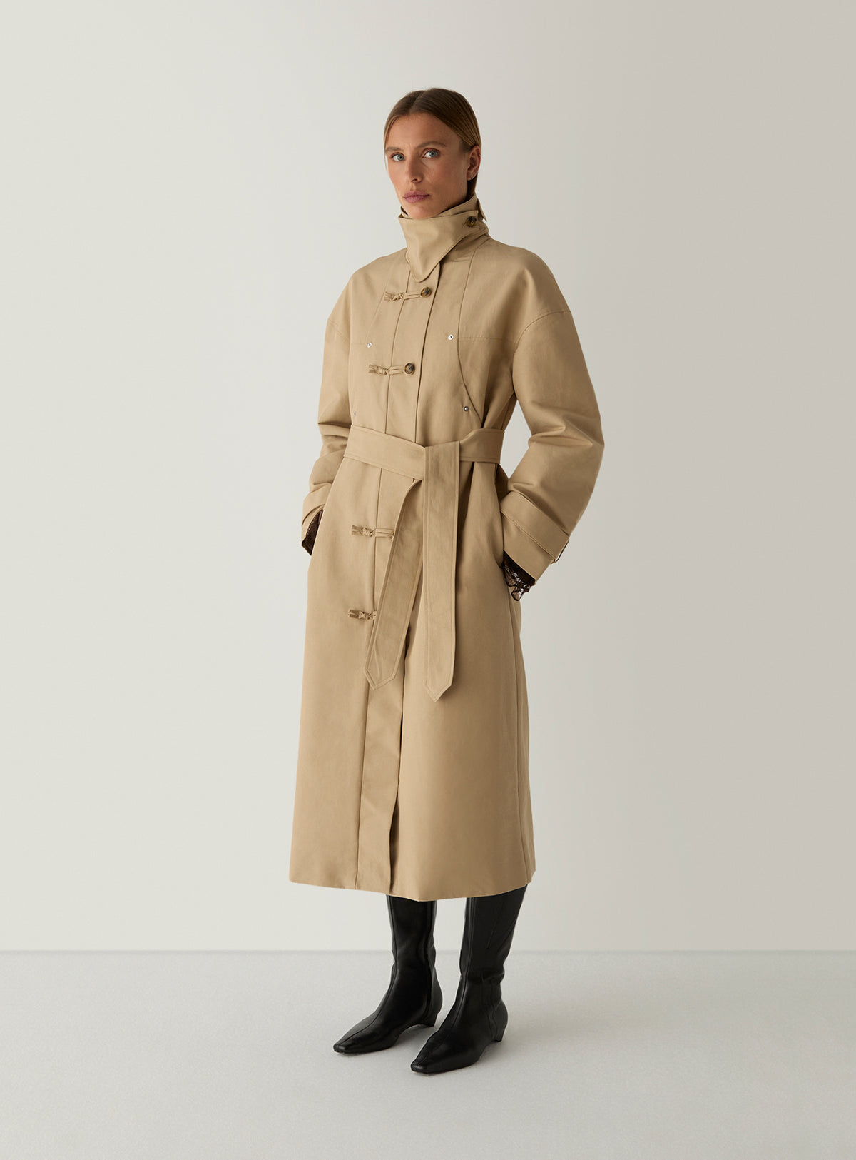Model in the camel Antwerp trench coat by LAAGAM, collar buttoned up and belt left untied, worn with black knee boots.