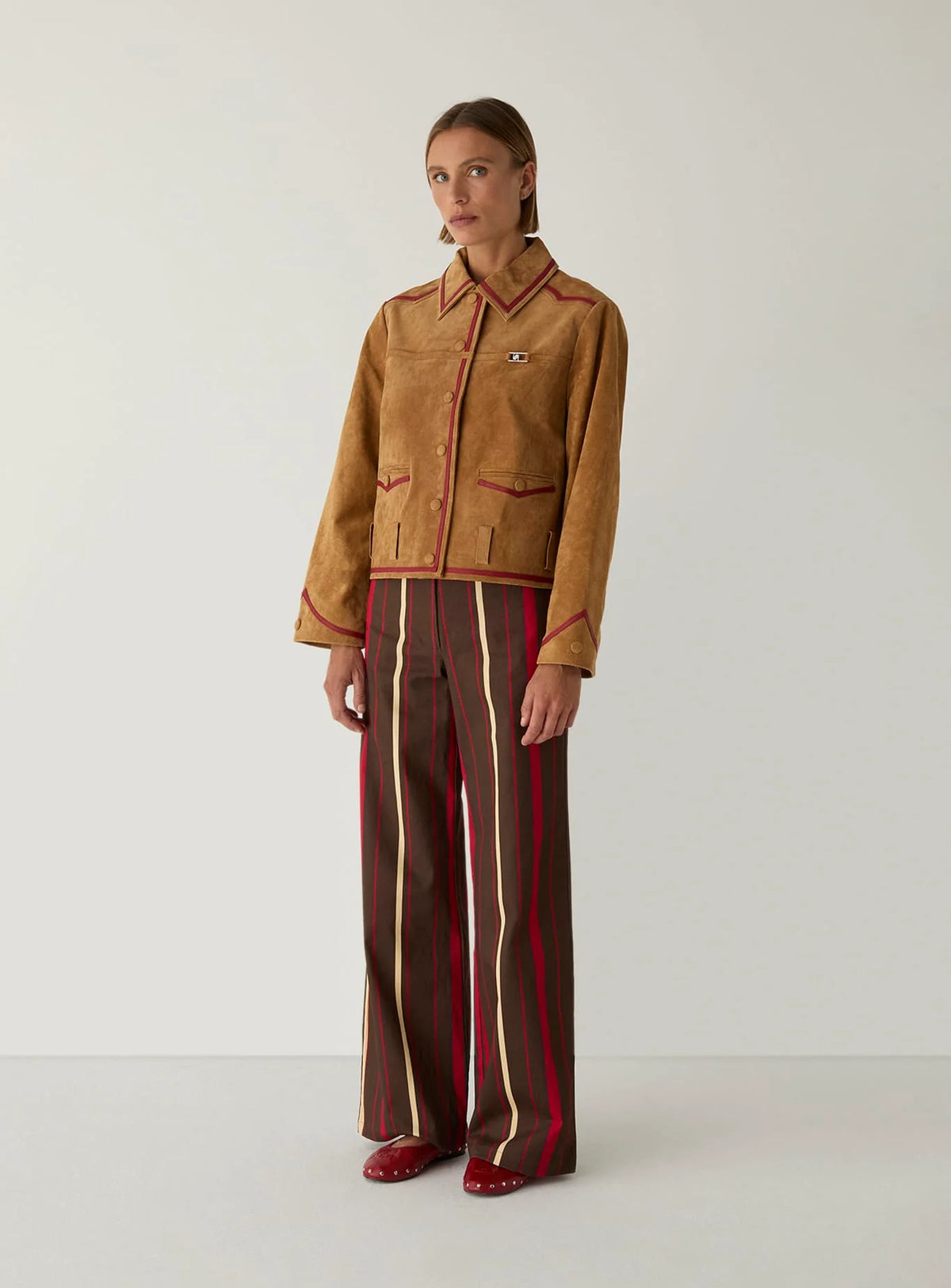 Full-length view of the LAAGAM Aveline camel suede jacket worn with striped wide-leg trousers and red flats.