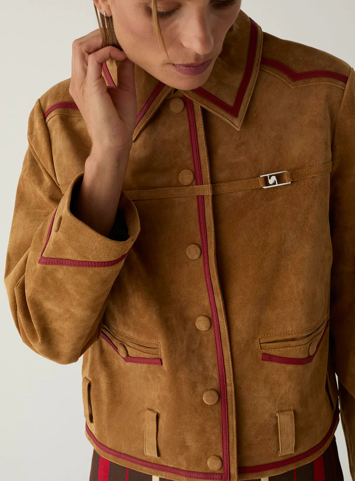 Close-up of the LAAGAM Aveline suede jacket, showing the self-covered snap buttons and red napa piping on the collar and cuff.