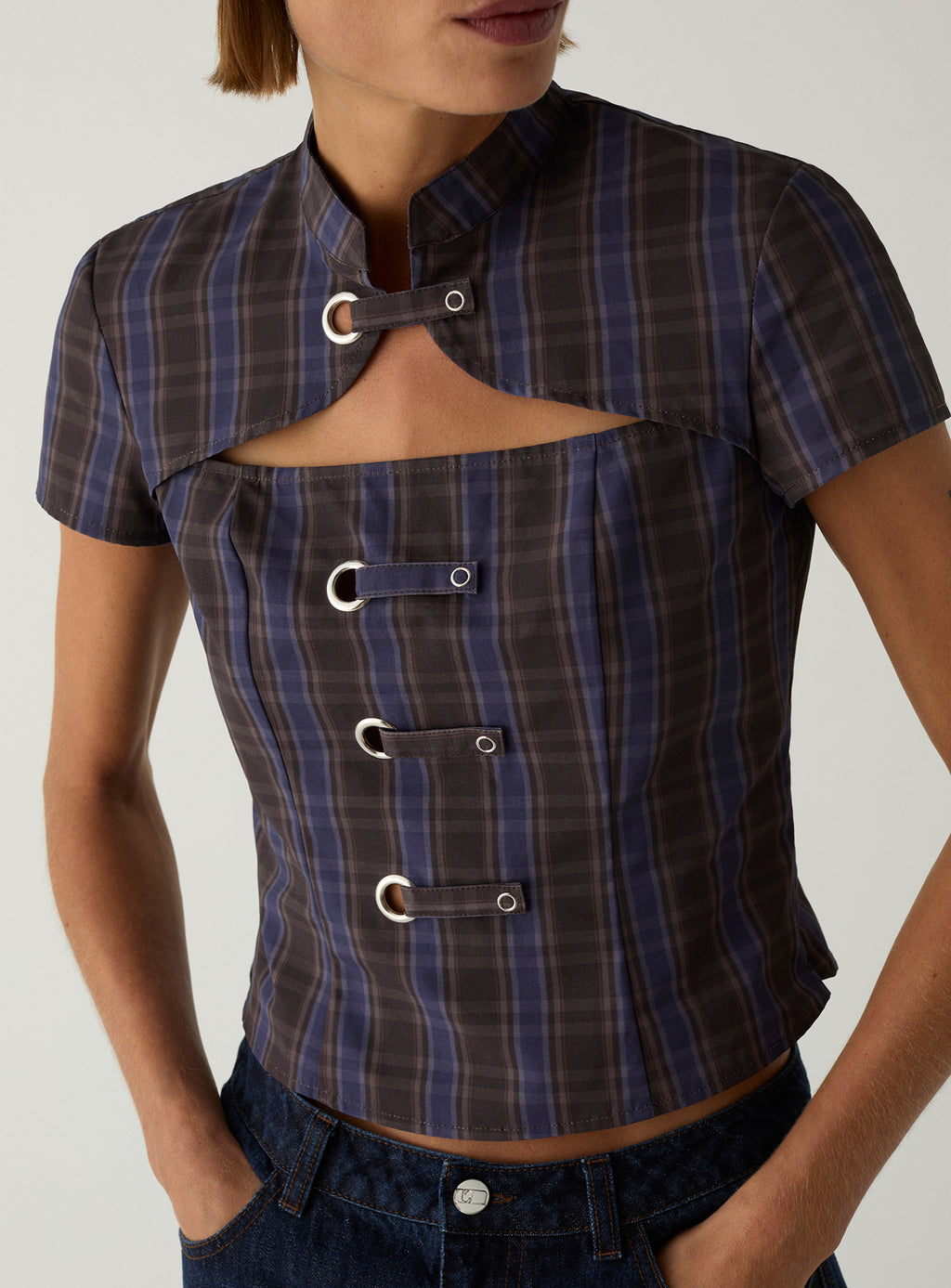 Close-up of the LAAGAM Azura cropped top in blue and brown check, with a high Mao collar, chest cut-out and eyelet tabs.