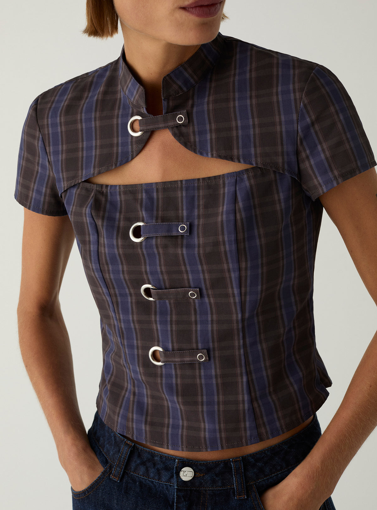 Close-up of the LAAGAM Azura cropped top in blue and brown check, with a high Mao collar, chest cut-out and eyelet tabs.