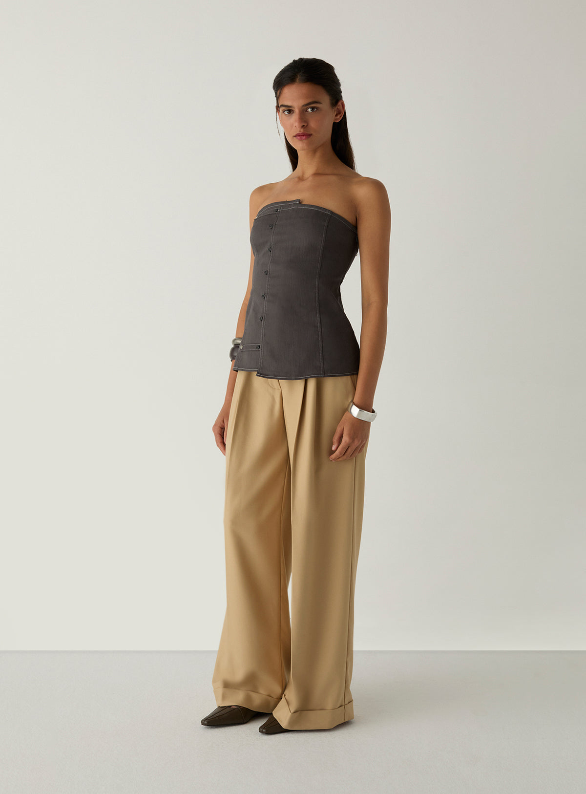 Model wearing the LAAGAM Lioren grey strapless top, styled with cream high-waisted wide-leg trousers.