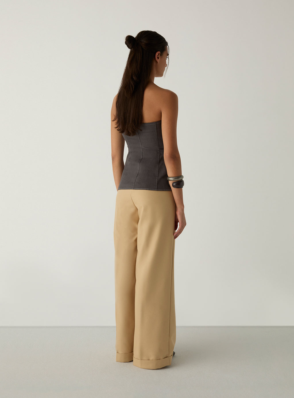 Back view of the LAAGAM Lioren grey strapless top, showing the curved seams that shape the back, with cream wide-leg trousers.