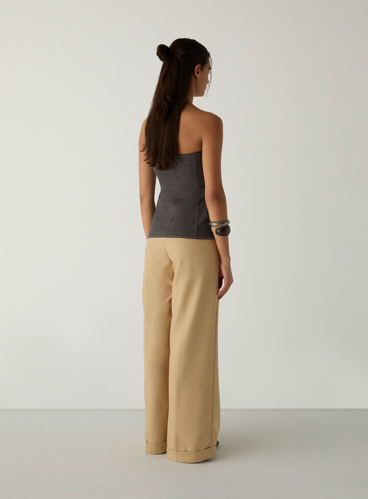 Back view of the LAAGAM Lioren grey strapless top, showing the curved seams that shape the back, with cream wide-leg trousers.