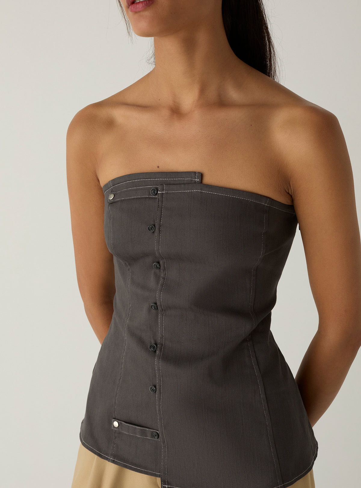 Front view of the LAAGAM Lioren grey strapless top, with its panelled fitted body, snap tab and curved asymmetric hem.