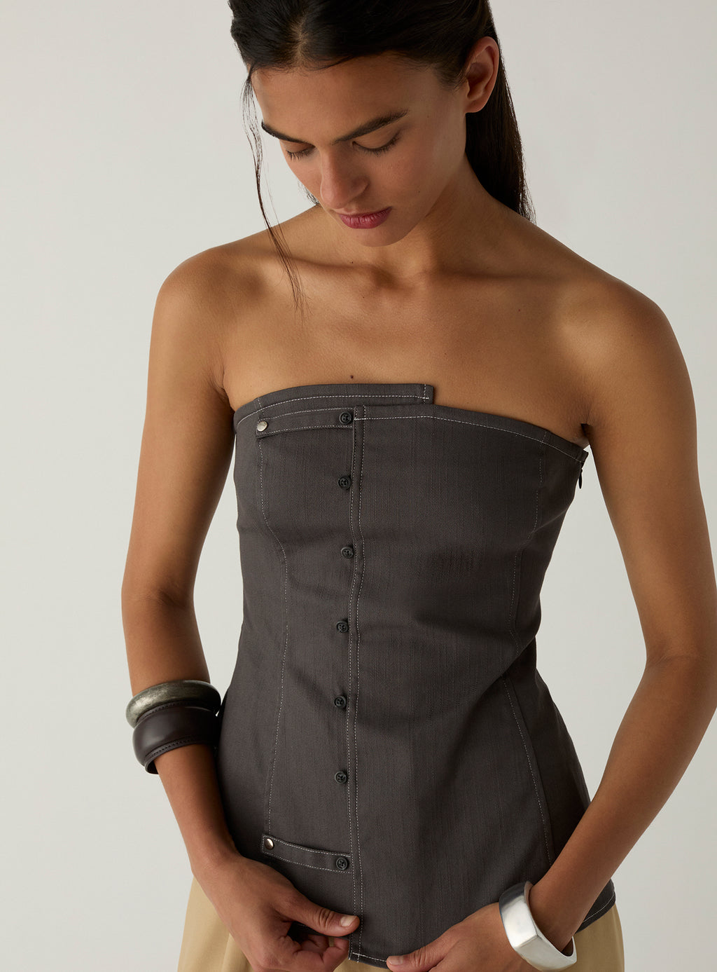Close-up of the LAAGAM Lioren grey strapless top, showing the asymmetric neckline, buttoned placket and contrast topstitching.