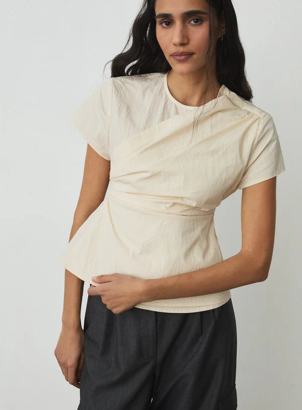 Woman wearing a beige top and dark pants against a plain background