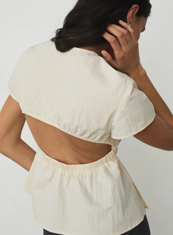 Woman wearing a cream-colored blouse with an open back design on a plain background