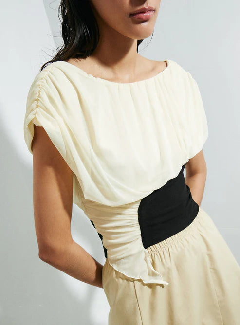 Woman wearing a top with a black and beige color block design against a white background