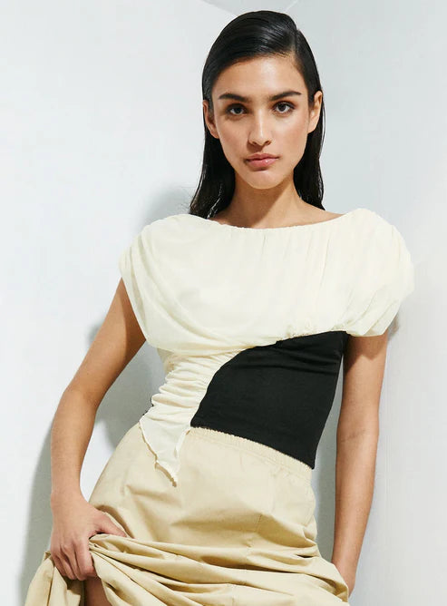 Woman wearing a top with a black and beige color block design against a white background