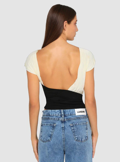 Back view of a woman wearing a black-and-white open-back top and blue jeans, standing against a plain light background.